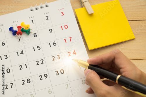 top view. hand of young woman using pen writing on desktop calendar and have post-it note putting on beside them. wooden are background. this image for business accessory concept