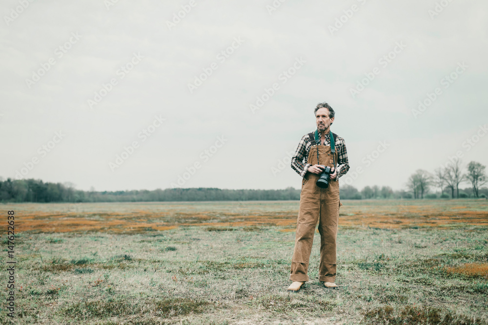 Nature photographer standing outdoor in grassy area.