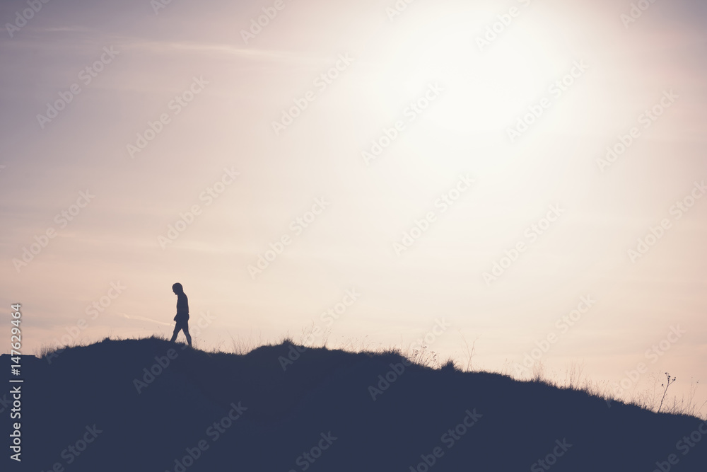 Fototapeta premium Man walking away from the sun on the hill. Artistic silhouette retro washout edit.
