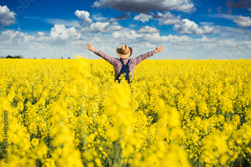 Agronomist standing in field of blooming cultivated rapeseed