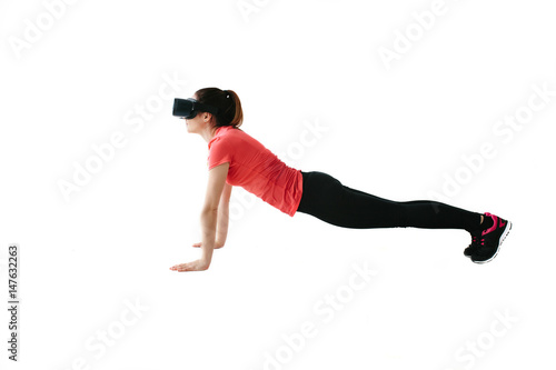 A young beautiful woman in virtual reality glasses makes aerobics remotely. Future technology concept. Modern imaging technology. Classes in single sports remotely. On a white background.
