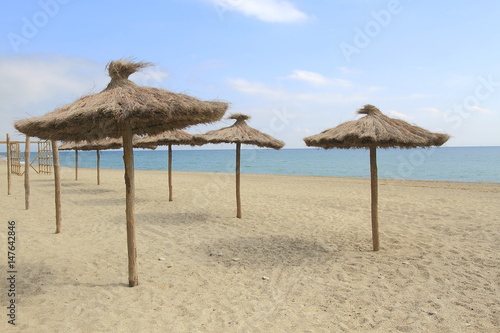 Parasols à la plage/Parasols en paille à la plage avec sable fin et ciel bleu