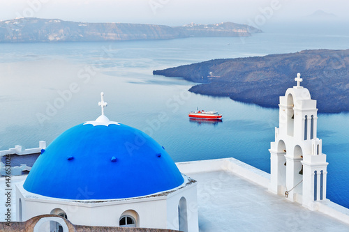 Blue dome church of Santorini island, Greece, Fira village. Island and moored red ferry in background, Morning scenery. 