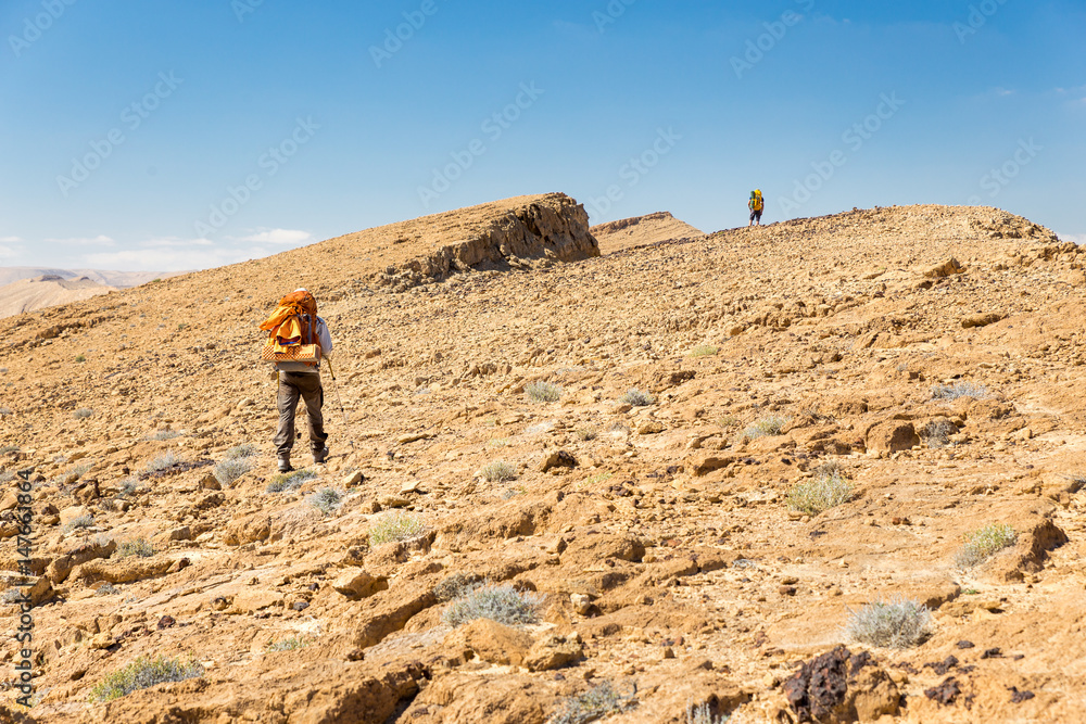 Two backpackers walking ascending mountain rock desert slope.