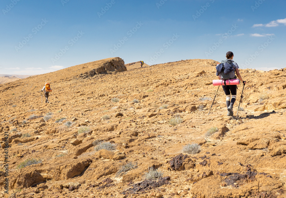 Three backpackers walking ascending mountain rock desert slope.