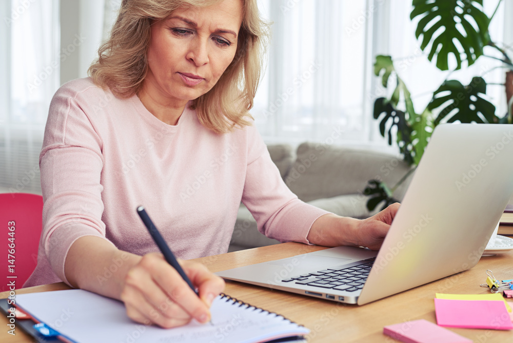 Concentrated madam writing while working in laptop Concentrated madam writing while working in laptop