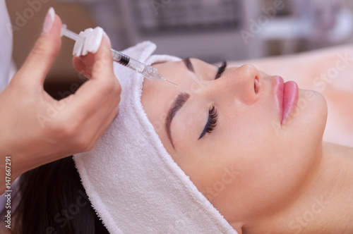 The doctor cosmetologist makes the Botulinotoxin injection procedure for tightening and smoothing wrinkles on the face skin of a beautiful, young woman in a beauty salon.Cosmetology skin care. photo