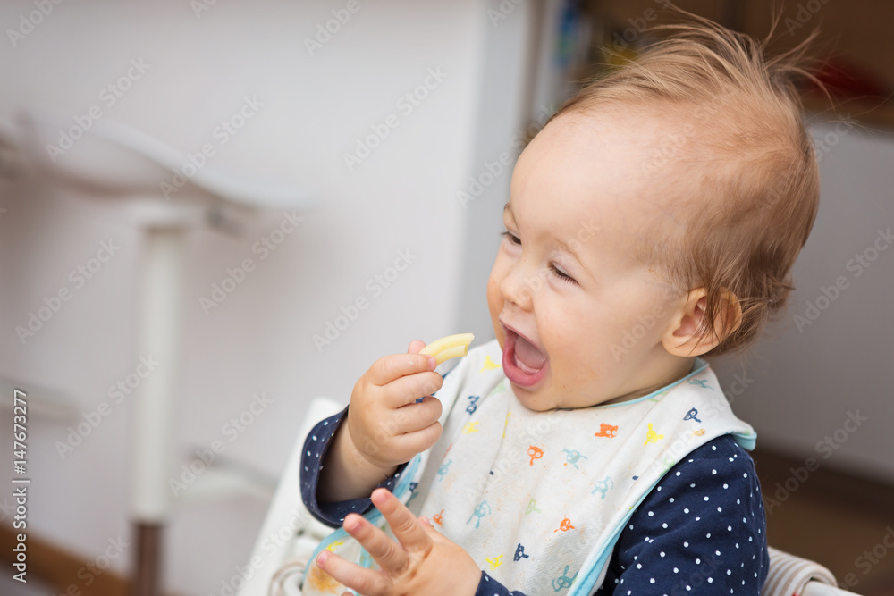 One year old baby girl feeding herself with her fingers, baby led weaning; concept of motherhood and parenting One year old baby girl feeding herself with her fingers, baby led weaning; concept of motherhood and parenting