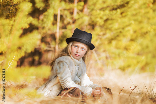 Cute beautiful girl with long hair in hat sits on clearing in spring forest.