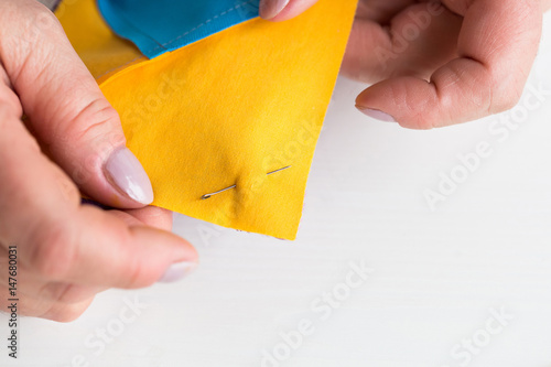 needlework and quilting at the workshop of a tailor woman on white background - close-up on the fingers of tailor fastened with the safety pin scraps of blue and yellow fabric for patchwor