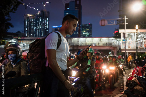 Young male tourist using the mobile phone while walking on a crowded street in Jakarta at night photo