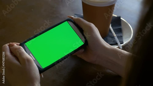 Woman watching a smart phone with chroma key green screen in landscape mode in a coffee shop