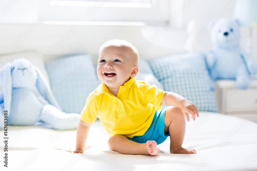 Baby boy playing on bed in sunny nursery Baby boy playing on bed in sunny nursery