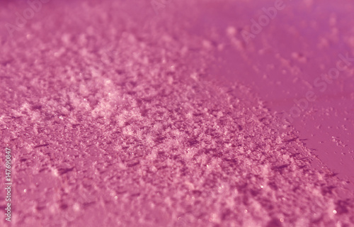 Snow on pink metal car surface with blur effect.