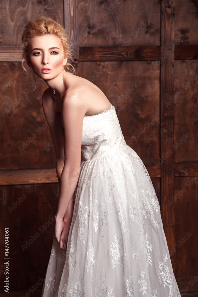 Fashion beauty bridal shooting. Beautiful fashion bride in wedding dress posing in front of woody background standing near brown leather sofa. studio shot in vogue style. Fashion beauty bridal shooting. Beautiful fashion bride in wedding dress posing in front of woody background standing near brown leather sofa. studio shot in vogue style.