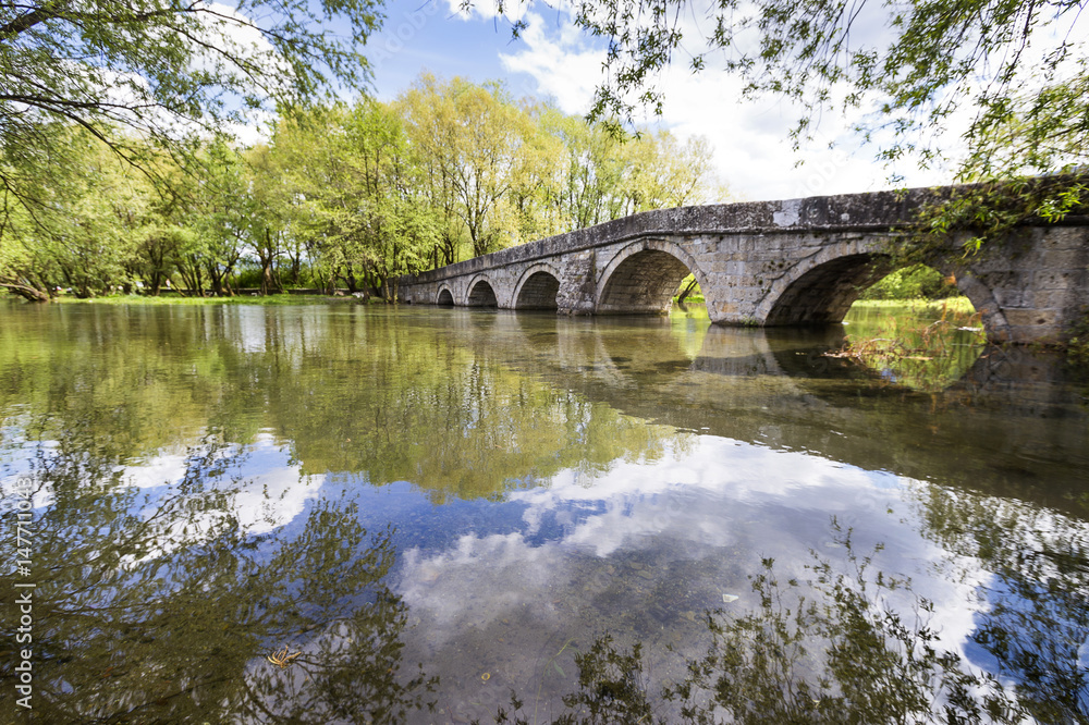 Old Roman bridge in Sarajevo on the river with reflection of the sky.