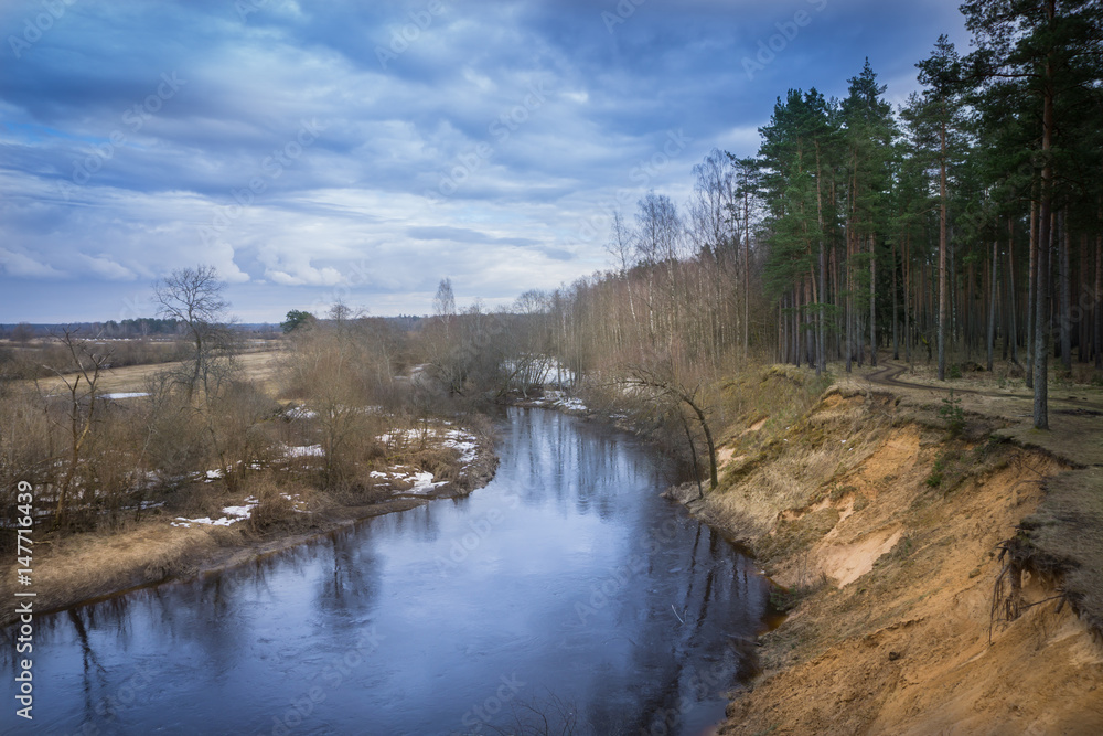 Latvian river with its bend in spring, with reflection of the sky and forest on water Latvian river with its bend in spring, with reflection of the sky and forest on water
