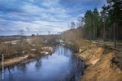 Latvian river with its bend in spring, with reflection of the sky and forest on water