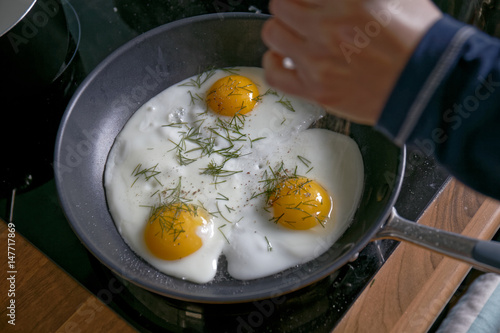 Fried eggs from a hen's egg in a frying pan with green dill leaves 