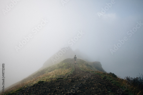 Man walking towards mountain peak in foggy weather