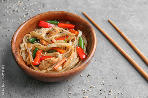 Wooden plate with delicious rice noodle and vegetables on grey background
