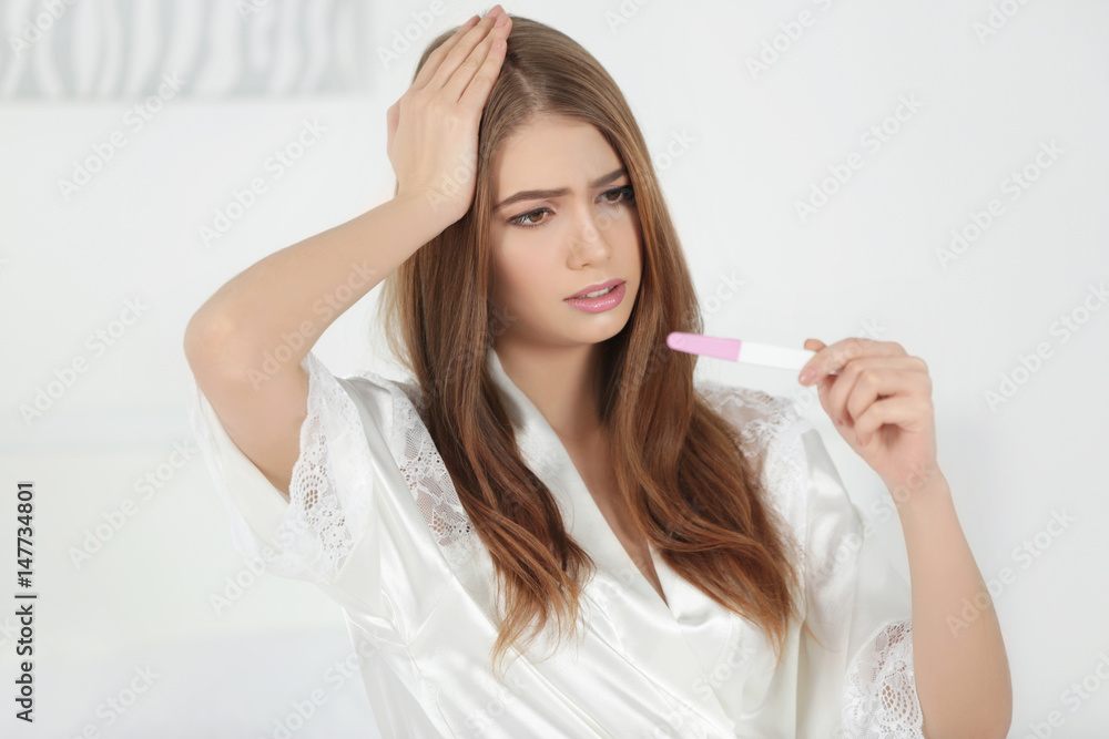 Beautiful young woman sitting on bed with pregnancy test Beautiful young woman sitting on bed with pregnancy test