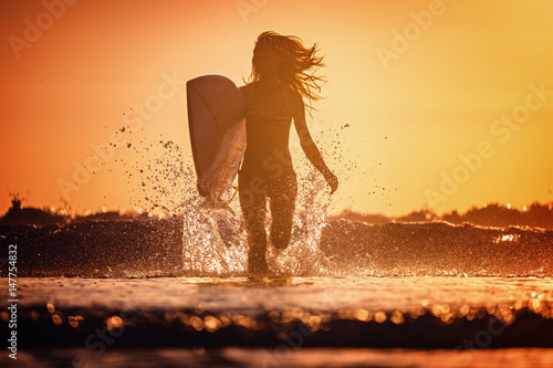 Young woman runs with surfboard with lots of splashes