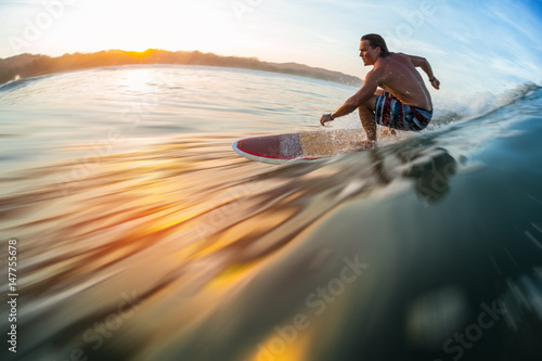 Surfer rides the ocean wave at sunrise