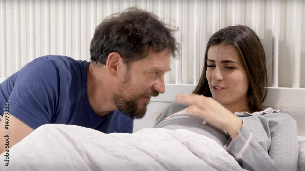Happy man and woman in bed expecting baby talking closeup Happy man and woman in bed expecting baby talking closeup