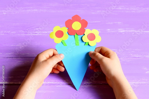 Small child made paper flowers crafts for mother's day or birthday. Child holds and shows a paper bouquet. Easy, quick and beautiful gift for mommy