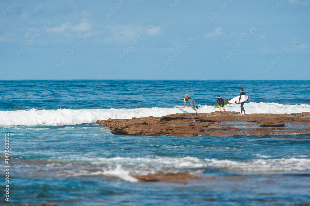 Surfers diving off the rocks to catch a wave