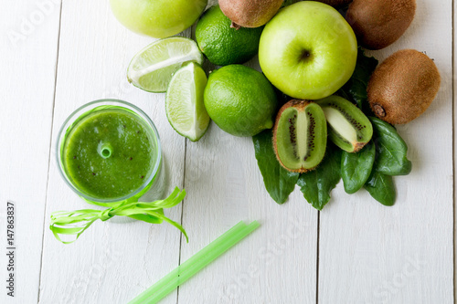 Green smoothie near ingredients for it on white wooden background. Apple, lime, spinach. Detox. Healthy drink. Top view.