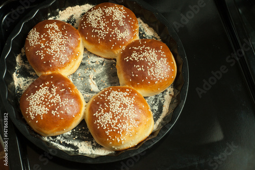 buns for burgers with sesame in a baking form on black background, copy space