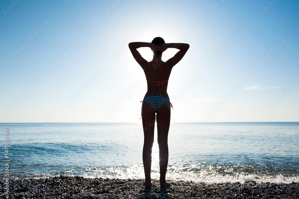 Young girl stretching herself on morning beach meeting the sunrise.