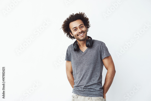 Happy african man with headphones on his nech listening to streaming music smiling looking at camera over white background. Flitrting with bypassing girls. photo