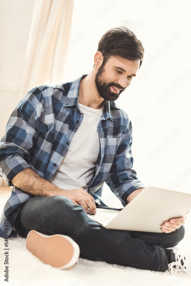 Fototapeta premium Man sitting on carpet and using laptop