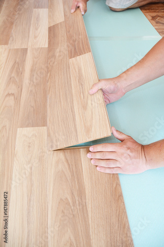 Contractor installing wooden laminate flooring with insulation and soundproofing sheets. Man laying laminate flooring. Man laying laminate flooring.