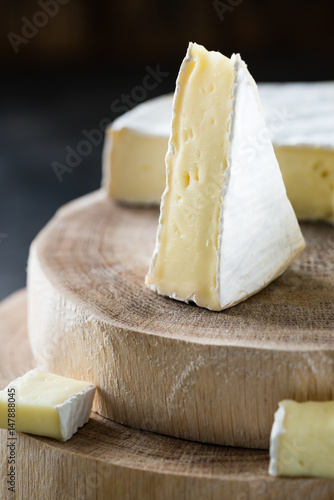 Closeup of soft cheese brie sliced on wooden cuts on dark rustic background