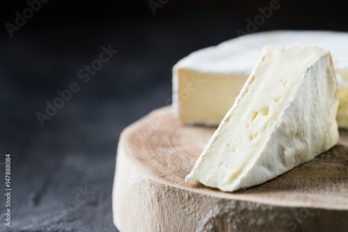 Closeup of soft cheese brie sliced on wooden cut on dark rustic background