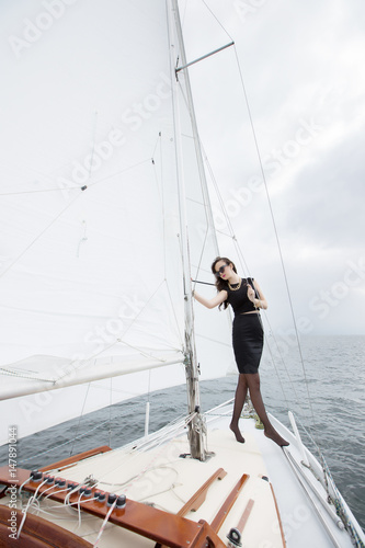 Portrait of a young cute brunette girl in a black dress posing on a yacht in the sea