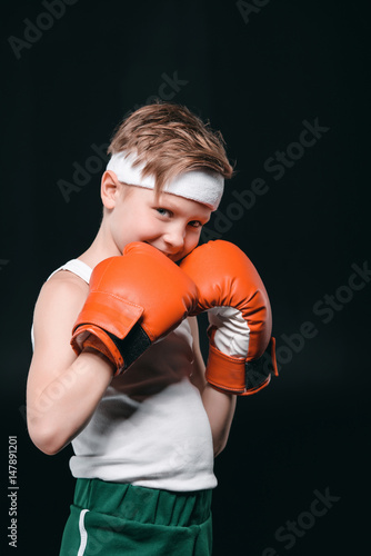 portrait of smiling boy in boxing gloves isolated on black, active kids concept © LIGHTFIELD STUDIOS