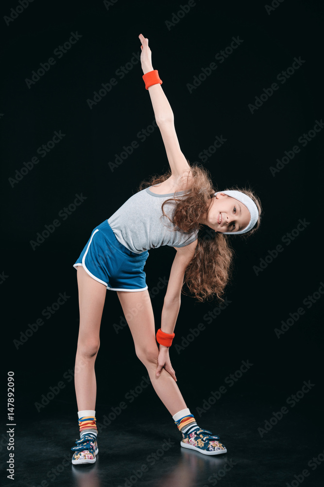 girl in sportswear exercising isolated on black. acting kids 12