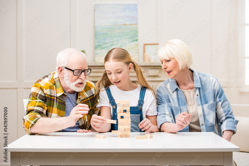 Cute little girl with grandfather and grandmother playing jenga game at home Cute little girl with grandfather and grandmother playing jenga game at home