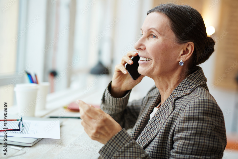 Profile view of cheerful senior woman talking to her friend on smartphone while enjoying coffee break in lovely cafe with panoramic windows, head and shoulders portrait Profile view of cheerful senior woman talking to her friend on smartphone while enjoying coffee break in lovely cafe with panoramic windows, head and shoulders portrait