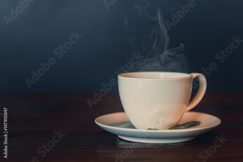 white hot coffee cup on wood table with smoke vapor on dark background vintage color tone.