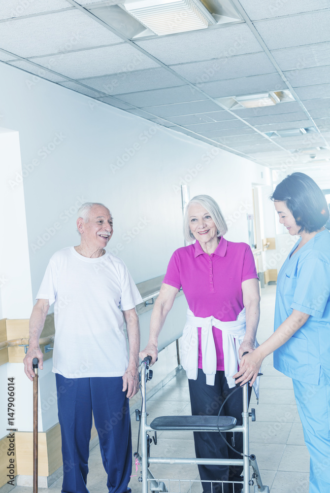 Fototapeta premium Happy elderly couple of seniors in rehab clinic helped by asian nurse