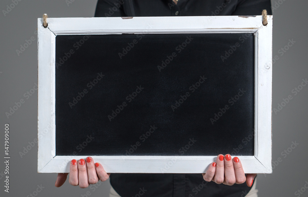 Obraz premium Hands holding empty chalkboard with a lot of free blank copy space for text. Woman showing blank blackboard against dark gray background. Nice template for design, artwork and marketing.