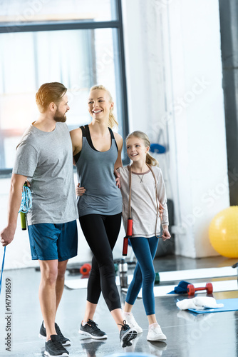 Young parents and daughter with skipping ropes at health club