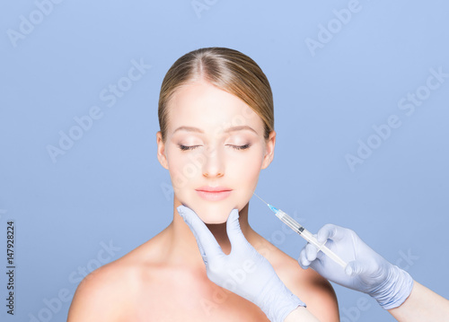Young and beautiful woman having skin injections over blue background. Plastic surgery concept.