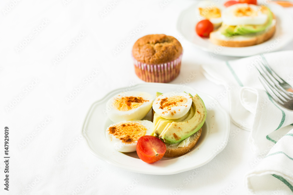 Healthy breakfast: toasts with avocado slices, tomato, paprika and eggs on white tableware. Selective focus